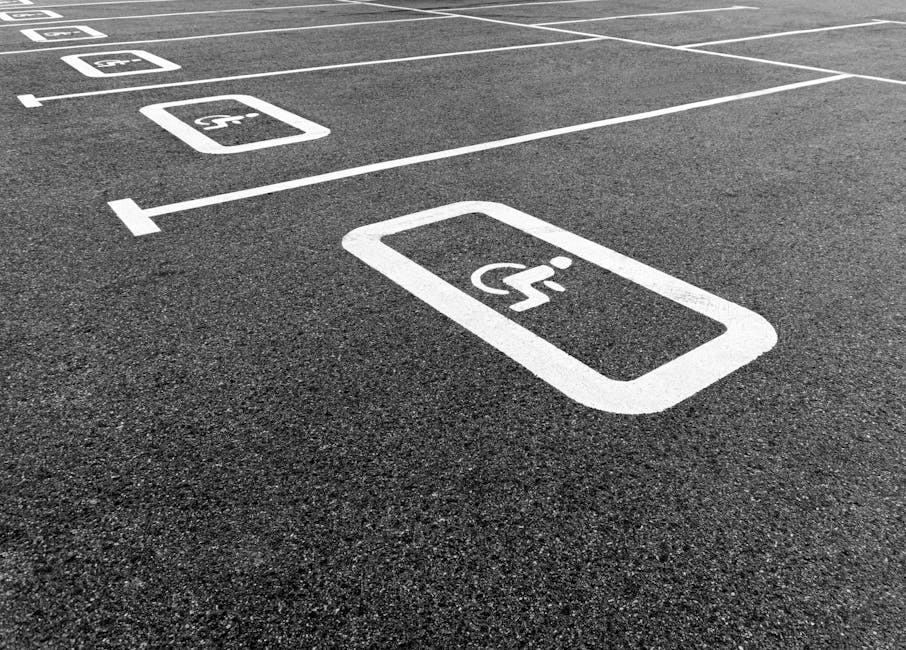 Close-up view of a designated accessible parking space on an asphalt surface, featuring a white wheelchair symbol painted within a rectangular outline. The space is part of a numbered parking lot, with adjacent markings indicating additional parking spots. The surface appears smooth and well-maintained, with clearly visible lines and symbols. This parking area is typical for accessible vehicle parking close to residential or commercial properties, and is relevant to moving services provided by Removal Companies Merton, especially when planning home relocations near Wimbledon Common. The image emphasizes the importance of accessible parking arrangements during furniture transport, packing, and loading processes involved in professional removals.