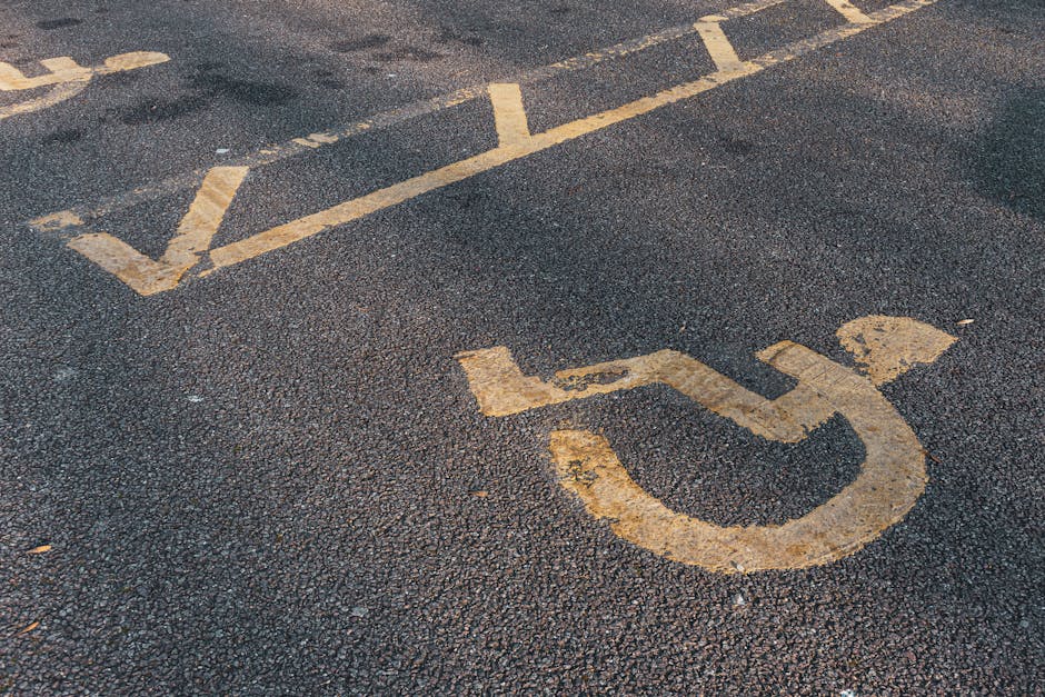 Close-up view of a designated accessible parking space on an asphalt surface, featuring a white wheelchair symbol painted within a rectangular outline. The space is part of a numbered parking lot, with adjacent markings indicating additional parking spots. The surface appears smooth and well-maintained, with clearly visible lines and symbols. This parking area is typical for accessible vehicle parking close to residential or commercial properties, and is relevant to moving services provided by Removal Companies Merton, especially when planning home relocations near Wimbledon Common. The image emphasizes the importance of accessible parking arrangements during furniture transport, packing, and loading processes involved in professional removals.